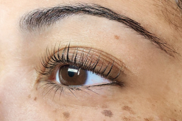 An extreme closeup of a Black woman’s brown eye with eyelashes that have received a lash lift service from The Lash Lounge.