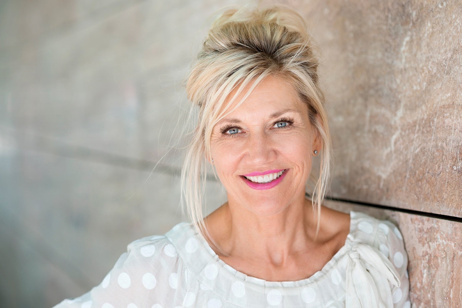 middle-aged blonde woman smiling and wearing pink lipstick and lash extensions