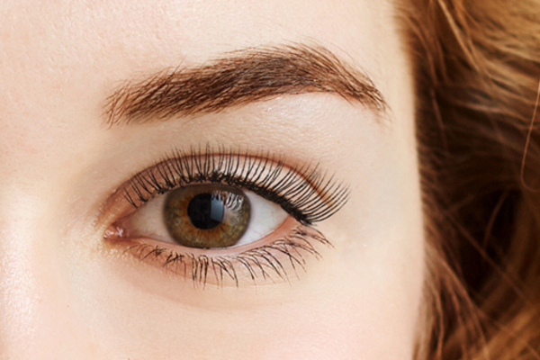 An extreme closeup of a Caucasian woman’s hazel eye and eyebrows after receiving a brow and lash tint service from The Lash Lounge.