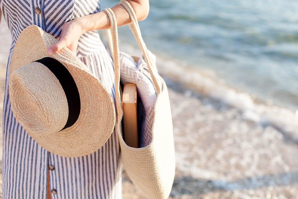 A woman in a striped dress walking on the beach with a beach bag