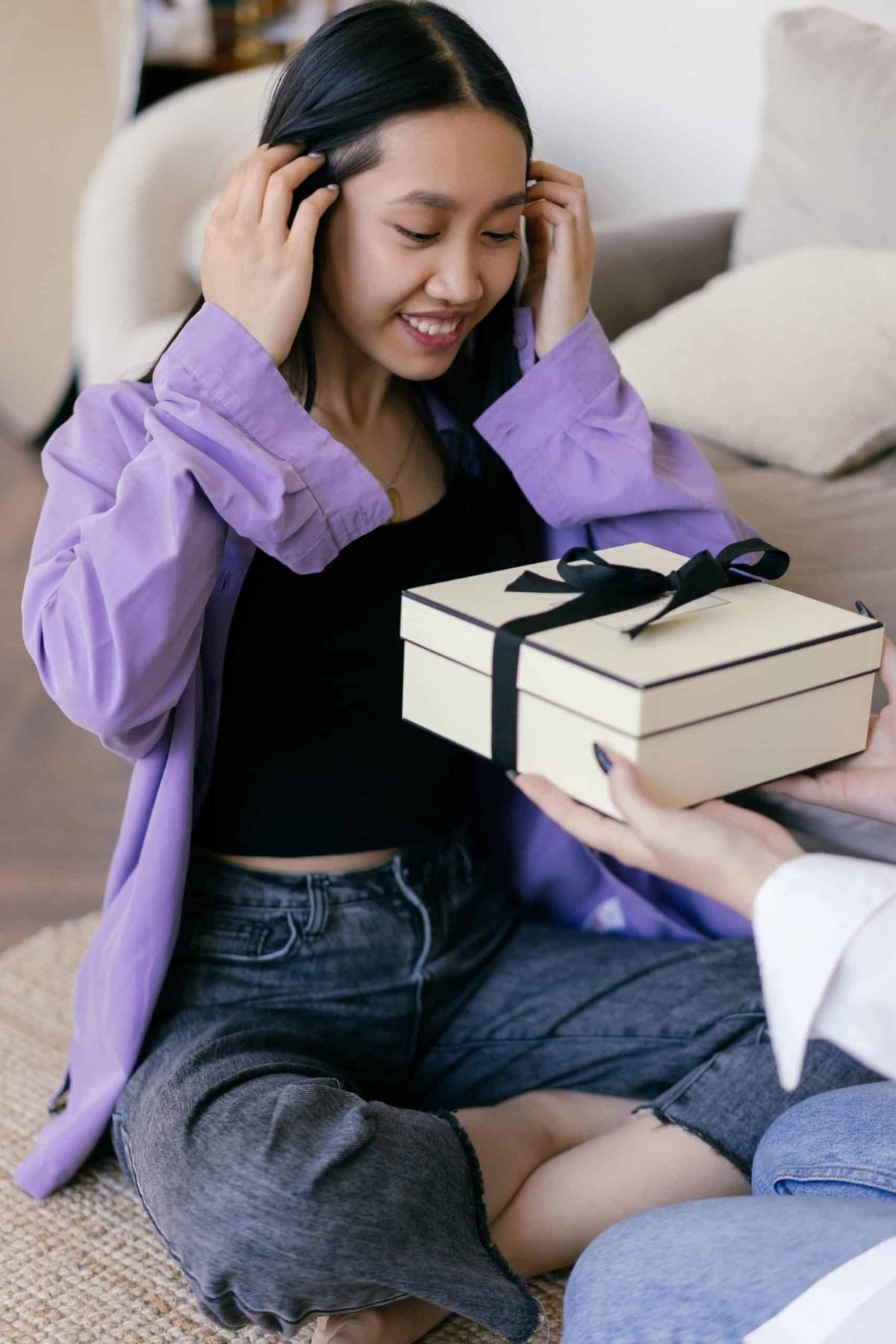 A woman sitting smiles as she is handed a holiday gift