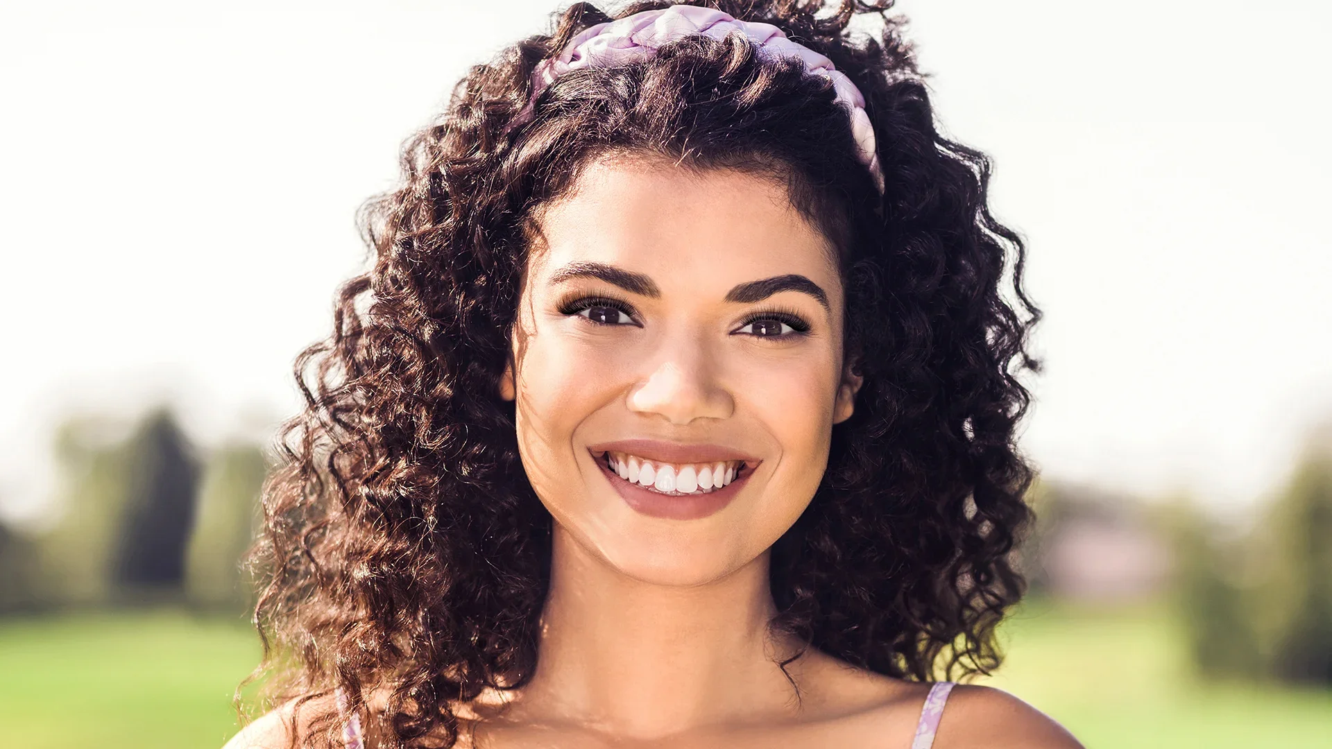 Midshot of biracial woman smiling outdoors with hybrid lash extensions 