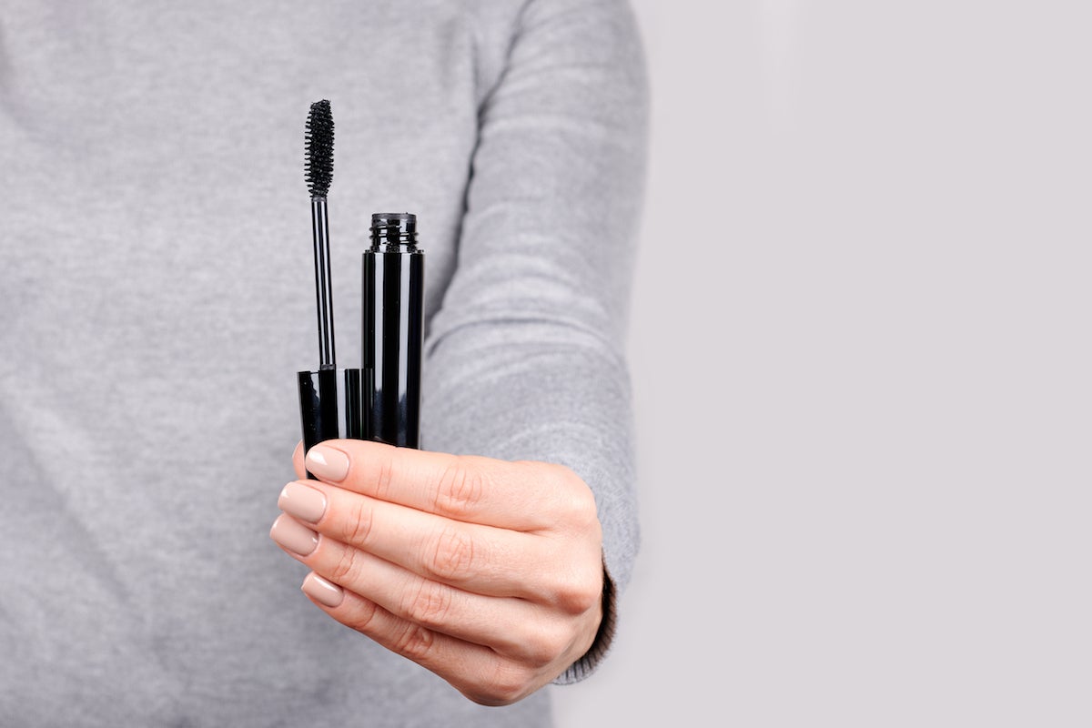 close-up of a woman's hand holding an open tube of mascara