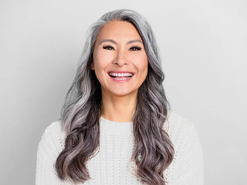 Mature woman with eyelash extensions smiling while wearing a sweater.