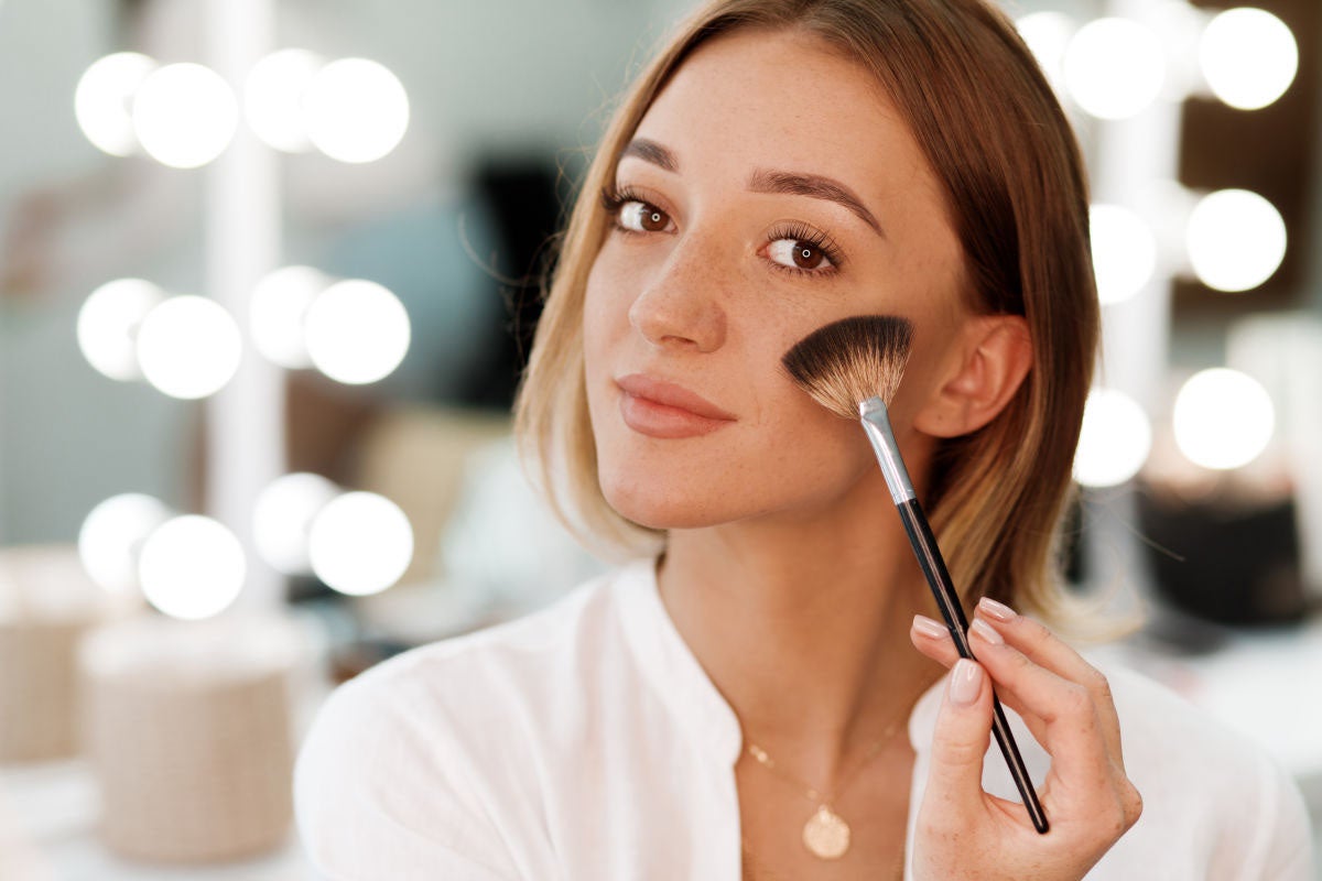 white woman applying makeup in mirror