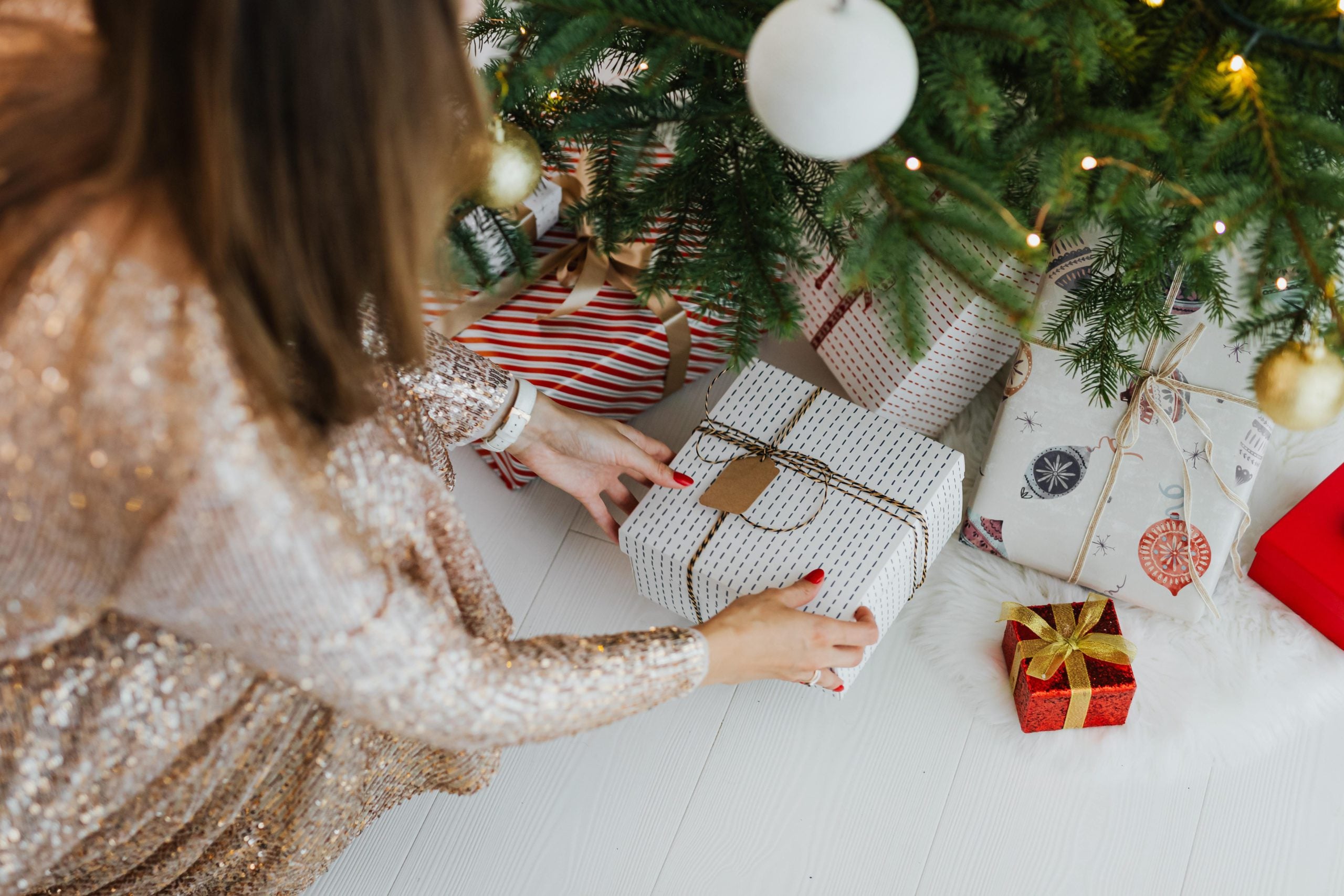 A woman reaches under a Christmas tree for a holiday gift