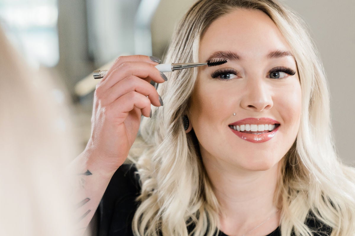 white woman brushing her brows in mirror