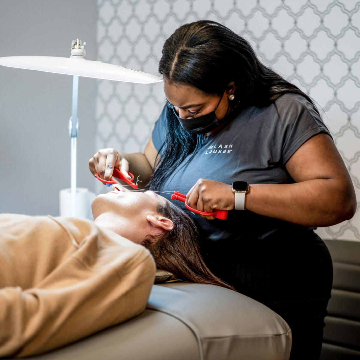 Lash Lounge stylist standing and threading guest's brow